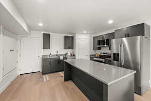 Kitchen featuring stainless steel appliances, a kitchen island, light wood-style floors, recessed lighting, and light stone countertops