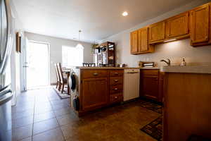 Kitchen featuring a peninsula, wood finish cabinetry, stainless steel fridge, light countertops, and white dishwasher