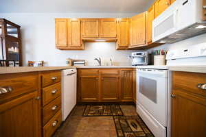 Kitchen with white appliances, light countertops, and wood finish cabinets