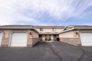 Traditional-style townhome with single car garages, stucco siding, covered porch, stone siding, and a shingled roof