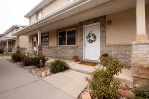 Doorway to property with a porch, stucco siding, and stone siding