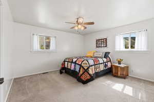Carpeted bedroom with multiple windows and ceiling fan