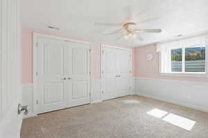 Unfurnished bedroom with a wainscoted wall, two closets, carpet flooring, and a ceiling fan