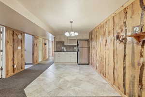 Kitchen featuring wood walls, dark countertops, hanging lights, freestanding refrigerator, and cream cabinetry