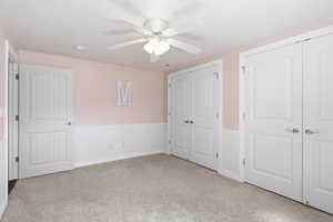 Unfurnished bedroom featuring a wainscoted wall, multiple closets, light colored carpet, and ceiling fan