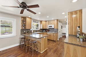 Kitchen with a peninsula, dark wood-type flooring, a breakfast bar area, light wood finish cabinetry, and recessed lighting