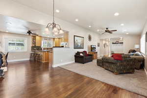 Living room featuring a ceiling fan, dark wood-style floors, and hanging lights
