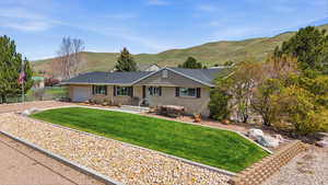 Ranch-style home featuring a mountain view, a garage, a front lawn, brick siding, and driveway
