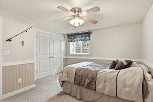 Carpeted bedroom with a wainscoted wall, a closet, ceiling fan, and a textured ceiling