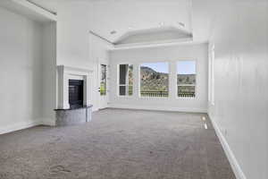 Unfurnished living room featuring carpet flooring, a glass covered fireplace, recessed lighting, lofted ceiling, and a raised ceiling