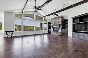 Unfurnished living room with a stone fireplace, built in features, dark wood-type flooring, lofted ceiling, and a ceiling fan