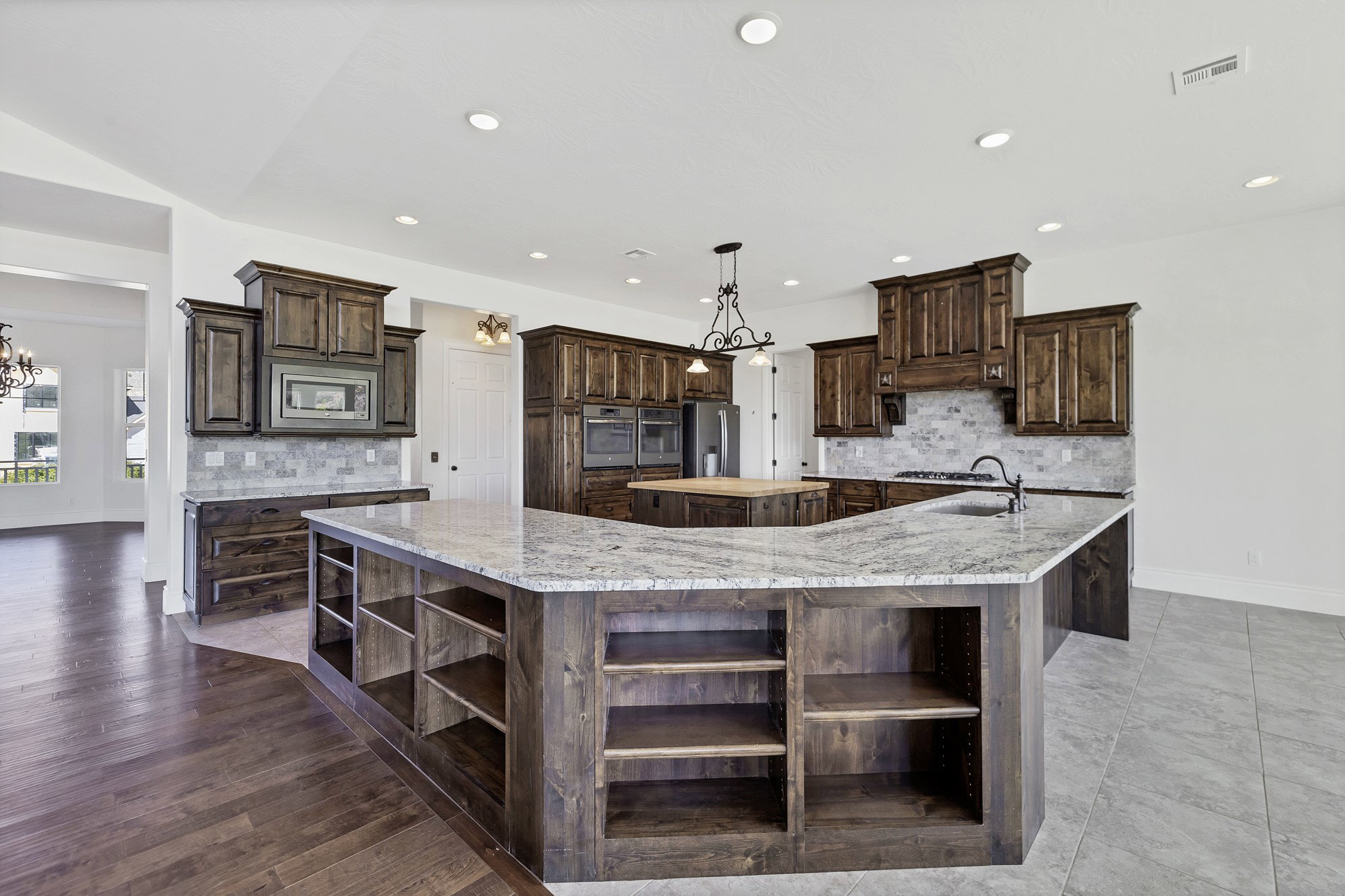Kitchen featuring open shelves, backsplash, dark wood finish cabinets, and a chandelier
