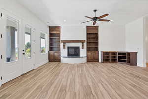 Unfurnished living room with ceiling fan, light wood-style floors, built in shelves, a glass covered fireplace, and recessed lighting