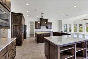 Kitchen featuring open shelves, dark wood finish cabinets, stainless steel appliances, ceiling fan, and light stone countertops
