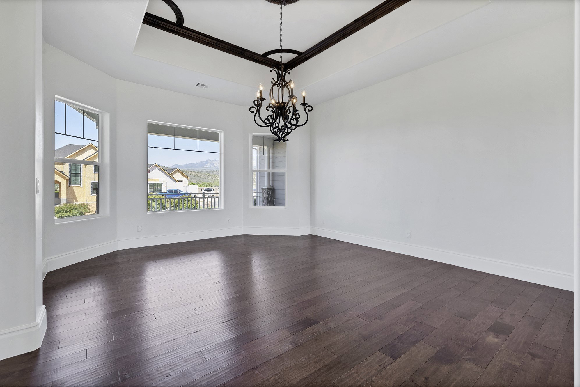 Unfurnished dining area featuring a raised ceiling, dark wood finished floors, a chandelier, and crown molding