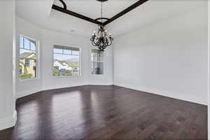 Unfurnished dining area featuring a raised ceiling, dark wood finished floors, a chandelier, and crown molding