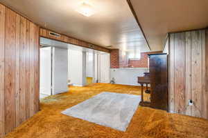 Living area with light colored carpet, wooden walls, and brick wall