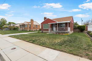 View of front facade with a porch, brick siding, a front yard, and a chimney