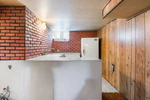 Kitchen featuring freestanding refrigerator, brick wall, and a peninsula