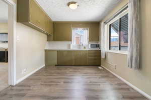 Kitchen featuring light wood-style flooring, healthy amount of natural light, tasteful backsplash, a textured ceiling, and white microwave