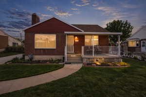 Bungalow-style home with covered porch, a yard, brick siding, and a chimney