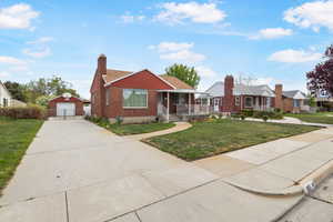 Bungalow-style home featuring an outdoor structure, a front lawn, a porch, a garage, and a chimney