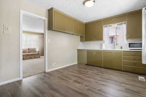 Kitchen with a textured ceiling, green cabinetry, light countertops, tasteful backsplash, and dark wood-style floors
