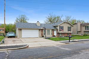 Tri-level home featuring concrete driveway, a chimney, a shingled roof, a front lawn, and an attached garage