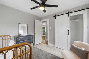 Bedroom with a barn door, light wood-style floors, and ceiling fan