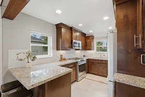 Kitchen with light stone counters, a kitchen bar, stainless steel appliances, a peninsula, and recessed lighting