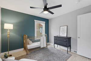 Bedroom with a nursery area, light wood finished floors, and ceiling fan