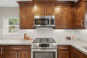 Kitchen with stainless steel appliances, light stone countertops, tasteful backsplash, and wood finish cabinetry