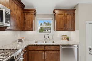 Kitchen with stainless steel appliances, light stone counters, wood finish cabinetry, and tasteful backsplash
