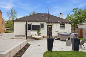 Rear view of property featuring a patio, brick siding, a chimney, and a hot tub