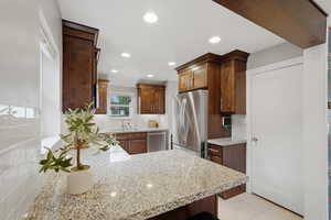Kitchen featuring tasteful backsplash, stainless steel appliances, a peninsula, light stone countertops, and recessed lighting