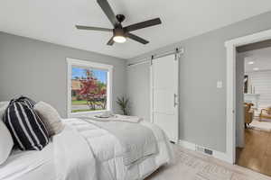 Bedroom featuring a barn door, light wood finished floors, and a ceiling fan