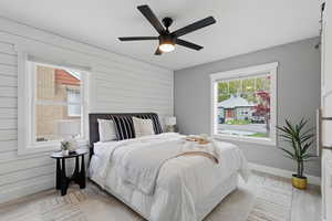Bedroom with light wood-style flooring, ceiling fan, and wooden walls