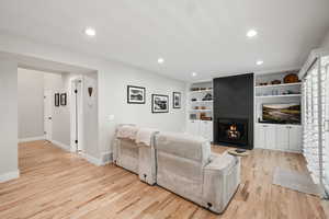 Living area featuring light wood-style flooring, a fireplace, recessed lighting, and built in shelves