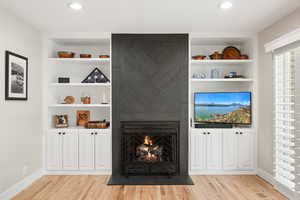 Living room with built in features, light wood-style floors, and a fireplace