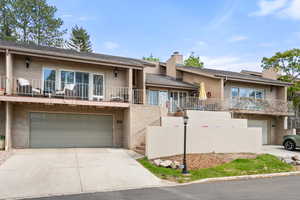 View of front of property with a garage, brick siding, a balcony, and driveway