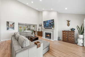 Living room with light wood-style floors, a high ceiling, recessed lighting, and a fireplace with flush hearth
