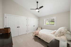 Bedroom with two closets, vaulted ceiling, carpet floors, and a ceiling fan