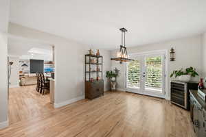 Dining room with light wood finished floors, wine cooler, and a chandelier