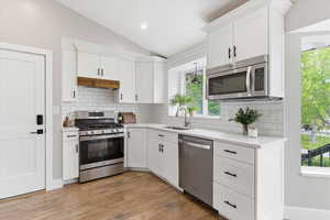 Kitchen featuring stainless steel appliances, lofted ceiling, white cabinetry, light wood-type flooring, and decorative backsplash