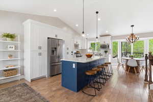 Dual tone kitchen with two tone color scheme, a center island with sink, stainless steel appliances, a kitchen breakfast bar, and light wood finished floors