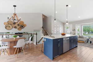 Kitchen with blue cabinetry, light wood finished floors, a kitchen island with sink, lofted ceiling, and a kitchen breakfast bar