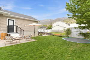 Fenced backyard featuring a patio, a mountain view, and a trampoline