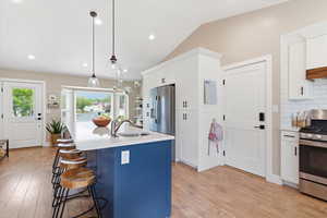 Two tone kitchen featuring a kitchen island with sink, a kitchen bar, stainless steel appliances, light wood finished floors, and dual tone cabinetry