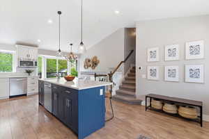 Kitchen with dual tone cabinetry, light wood-style flooring, a center island with sink, pendant lighting, and stainless steel appliances