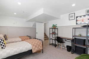 Bedroom with a decorative wall, wainscoting, and light colored carpet